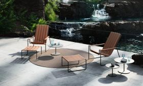 Zwei STRAPPY-195 Loungers in Braun mit Fußstützen und BUTLER-40TL-60T Beistelltischen auf einer Terrasse vor einem Wasserfall.
